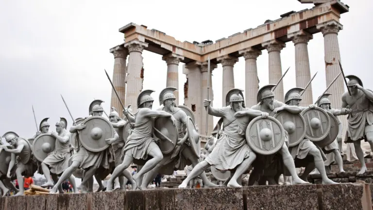 Statues of Greek soldiers in battle around a broken temple.