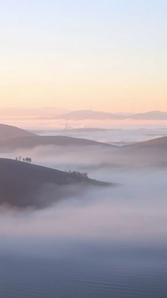 Misty rolling hills at dawn with pastel colors and a subtle hazy effect.
