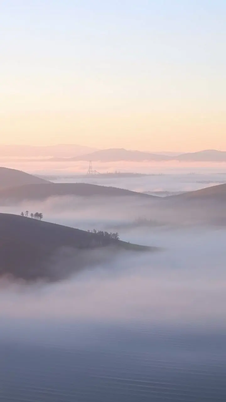 Misty rolling hills at dawn with pastel colors and a subtle hazy effect.