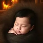 Newborn baby boy sleeping in fur by firelight