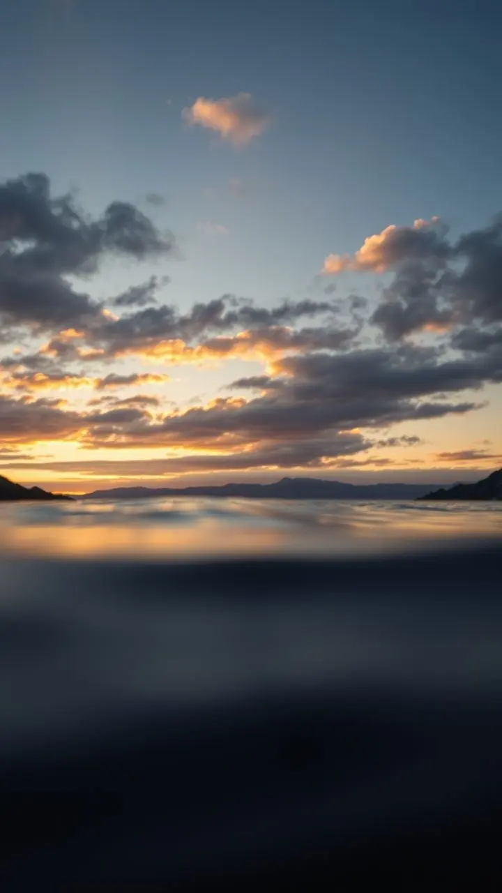 Sunset reflections on water with trees and mountains.