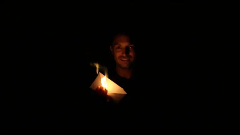 Man in dark room holding a burning envelope.
