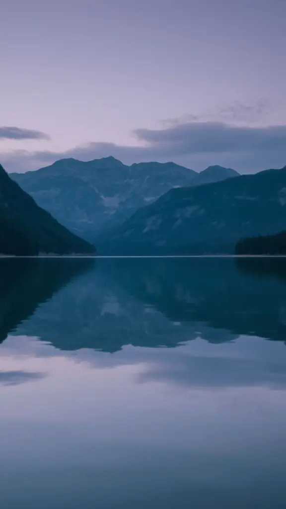 Lake reflection at twilight with mountains and forest.